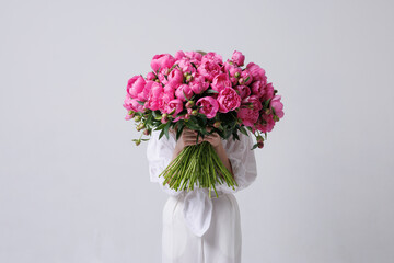Stylish woman with head covered in pink peonies posing in white outfit against a minimal background, artistic floral fashion concept.