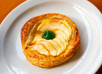 On plate is round little dessert - apple pie made of puff pastry with slices of natural...