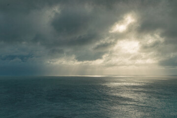 Fototapeta premium Lighthouse on the rockHeavy storm clouds over the sea with rays of sunshine