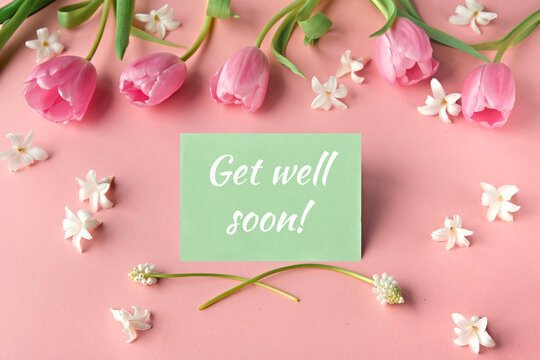 Pink tulips and white flowers on a pastel pink background with a green card displaying the text Get well soon