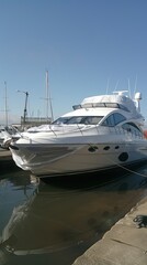 Fototapeta premium White yacht docked in harbor, sunny day, other boats visible