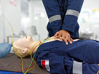 Close-up of middle-aged Asian male hands performing cardiopulmonary resuscitation (CPR) on a training dummy. Vital techniques include defibrillation, chest compressions, and maintaining the airway.

