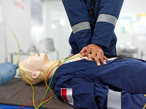 Close-up of middle-aged Asian male hands performing cardiopulmonary resuscitation (CPR) on a training dummy. Vital techniques include defibrillation, chest compressions, and maintaining the airway.
