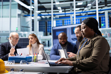 Shareholders in production plant doing doing research on laptops. Investors and factory management coworkers in office analyzing strategies for renewable energy equipment manufacturing expansion © DC Studio