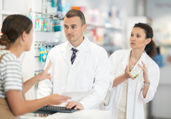 Man and woman pharmacists looking for prescription medicine for young woman using computer