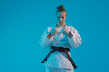 Female martial artist in a white gi with a black belt practicing a controlled move against a blue background