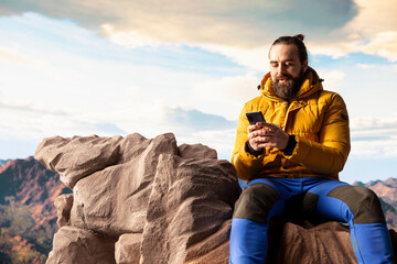 Nature lover relaxing on mountain top getting online with his phone at a scenic viewpoint, looking...