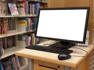 A public computer station in a library with a blank monitor screen, keyboard, and mouse on a wooden desk, surrounded by bookshelves filled with books.