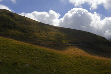 Mountain hillside with dramatic light and cloud shadows. Natural highland landscape with grassy slopes under a partly cloudy sky in remote outdoor setting