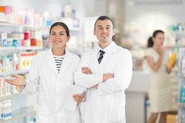 Fototapeta premium Positive young male and female pharmacists posing together in chemist's shop with large assortment