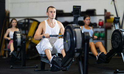 Young athletic man in sportswear training on rowing machine in gym..