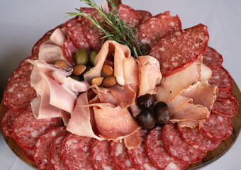 Gourmet catering for welcome cocktail. Closeup view of a cold cuts board with a white background. The plate presents prosciutto, ham, salami, olives and almonds.