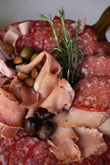 Gourmet catering for welcome cocktail. Closeup view of a cold cuts board with a white background. The plate presents prosciutto, ham, salami, olives and almonds.