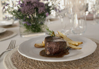 Gourmet gastronomy. Wedding main course. Closeup view of grilled loin tournedo with a red wine sauce and potatoes on the table with a beautiful glassware and tableware arrangement	
