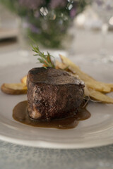 Gourmet gastronomy. Wedding main course. Closeup view of grilled loin tournedo with a red wine sauce and potatoes on the table with a beautiful glassware and tableware arrangement	
