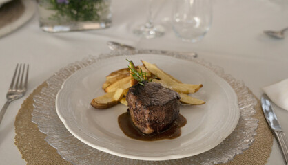 Gourmet gastronomy. Wedding main course. Closeup view of grilled loin tournedo with a red wine sauce and potatoes on the table with a beautiful glassware and tableware arrangement	
