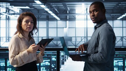 Data scientists in server room using laptop and tablet, executing security patches, verifying...