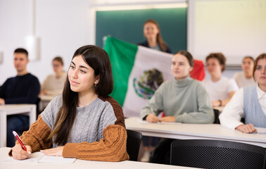 Female teacher tells her classmates about the country of Mexico, holding a flag in her hands