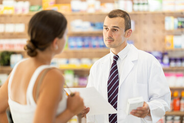 Polite male pharmacist consulting young girl about medicament in box in chemist's shop