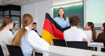 Obraz premium High school teacher holds the flag of Germany in her hands and talks about this country in a geography lesson