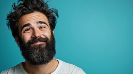 Obraz premium Close-up studio shot of a young man with a full, dark beard. His hair is dark and slightly disheveled. He is looking upward with a pensive yet happy expression. The background is a solid teal color.