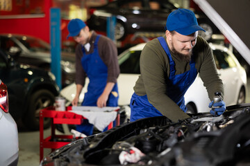 Fototapeta premium Proficient car mechanic in blue uniform checking auto-details in auto repair shop