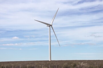 Fototapeta premium A large wind turbine stands against a partly cloudy blue sky, generating renewable energy in a vast open landscape