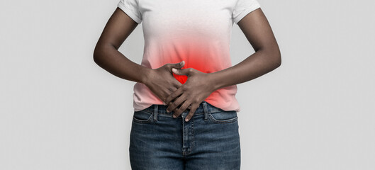 Sad black girl touching her belly, having stomachache, grey background