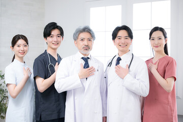 カッコイイグレイヘアの医者と複数のドクターのイメージ　笑顔のカメラ目線でお任せのポーズ　信頼と信用