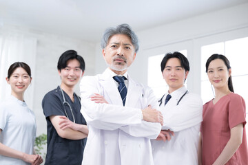 Image of a doctor with cool gray hair and multiple doctors looking at the camera with serious, serious arms folded.