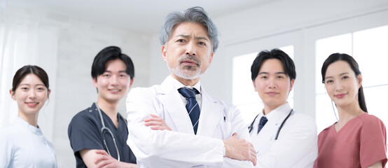 Fototapeta premium カッコイイグレイヘアの医者と複数のドクターのイメージ 真剣な真面目な腕組のカメラ目線のバナー