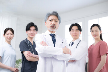 カッコイイグレイヘアの医者と複数のドクターのイメージ　真剣な真面目な腕組のカメラ目線
