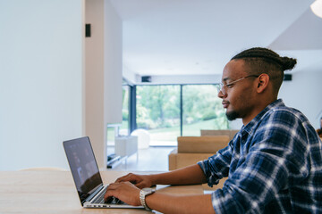 African American influencer in glasses sitting at a table in a modern living room, using a laptop for business video chat, conversation with friends and entertainment.