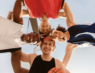 Smiling basketballers putting their heads together in unity outdoors, bottom view