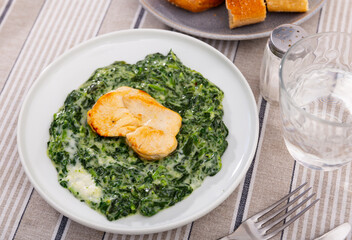 Healthy dinner of baked chicken fillet slices served with spinach stewed in thick and luscious white bechamel sauce..