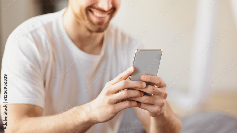 Poster unrecognizable smiling man using smartphone mobile app sitting in bedroom at home, focus on phone. g