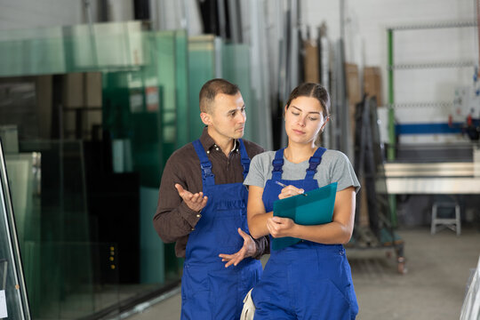 Two glass workshop workers in uniform discussing documents
