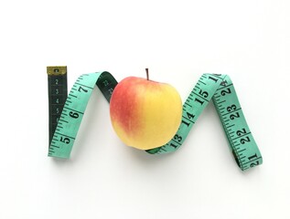 Ripe yellow apple and green measuring tape on white background