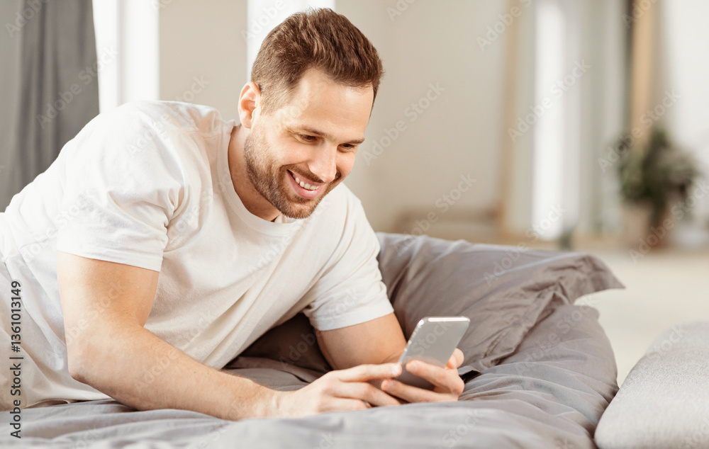 Aufkleber Mobile App. Cheerful Guy Using Smartphone Lying In Bed In Bedroom At Home. Man Browsing Internet On Phone. Application For Cellphone Advertisement. Free Space For Text
