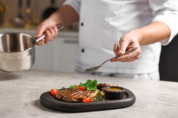 Professional chef adding sauce to delicious dish at table indoors, closeup