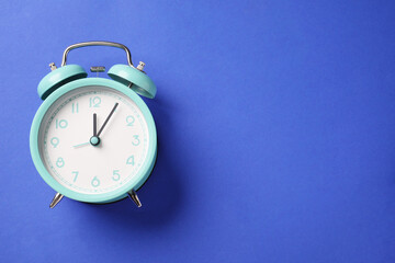 One turquoise alarm clock on blue background, top view. Space for text