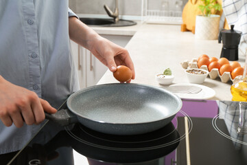 Woman breaking egg into frying pan in kitchen, closeup