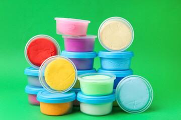 Different colorful modeling clay in plastic jars on green background
