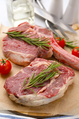 Pieces of raw beef, rosemary and tomatoes on table, closeup