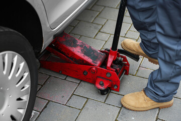 Fototapeta premium Auto mechanic lifting car with scissor jack outdoors, closeup