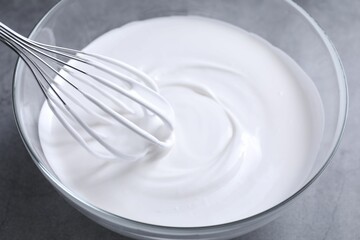 Mixing whipped cream in bowl with whisk on grey table, closeup