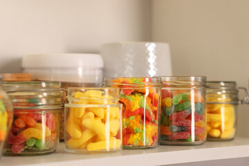 Tasty gummy candies in jars on shelf, closeup