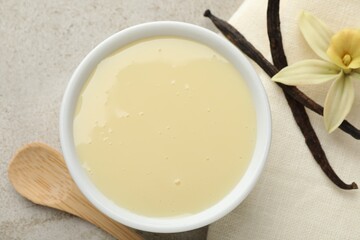 Tasty condensed milk, vanilla pods, flower and spoon on light grey table, flat lay