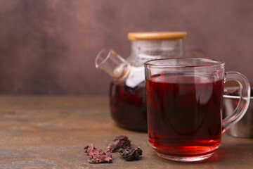Delicious hibiscus tea in glass cup, teapot and dry roselle sepals on wooden table, closeup. Space for text