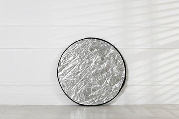 Professional reflector on floor near white wall. Photo studio equipment
